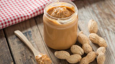 peanut butter in a jar with peanuts scattered around it