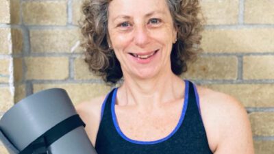 Karen Menis smiling, holding a yoga mat