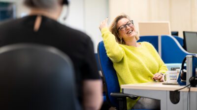 Woman seated at desk chair smiling at her coworker