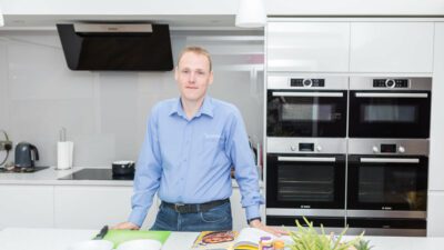 David standing in a blue shirt in a white kitchen with healthy ingredients on the table