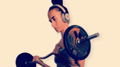 A slim woman holding a barbell listening to headphones.