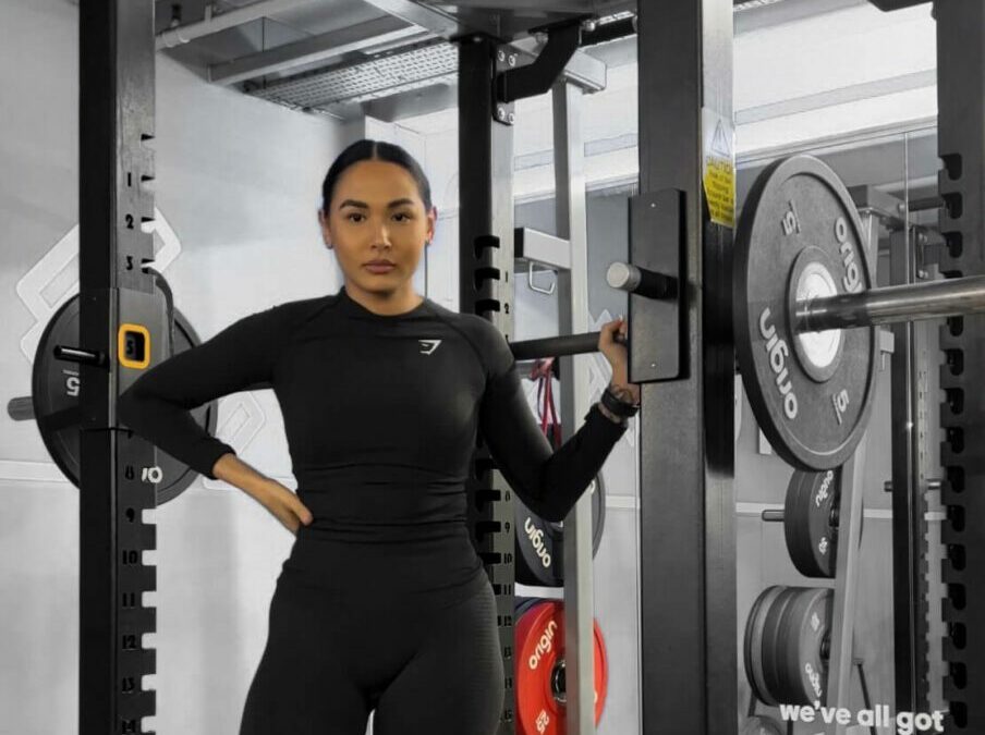 A woman standing in a squat rack holding a barbell