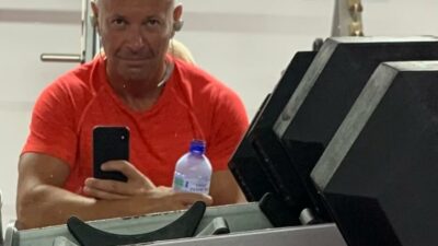 Mark leaning on gym equipment wearing an orange t-shirt