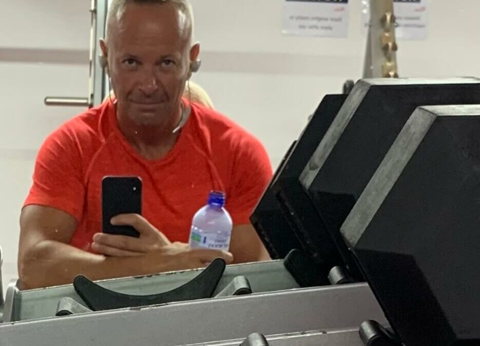 Mark leaning on gym equipment wearing an orange t-shirt