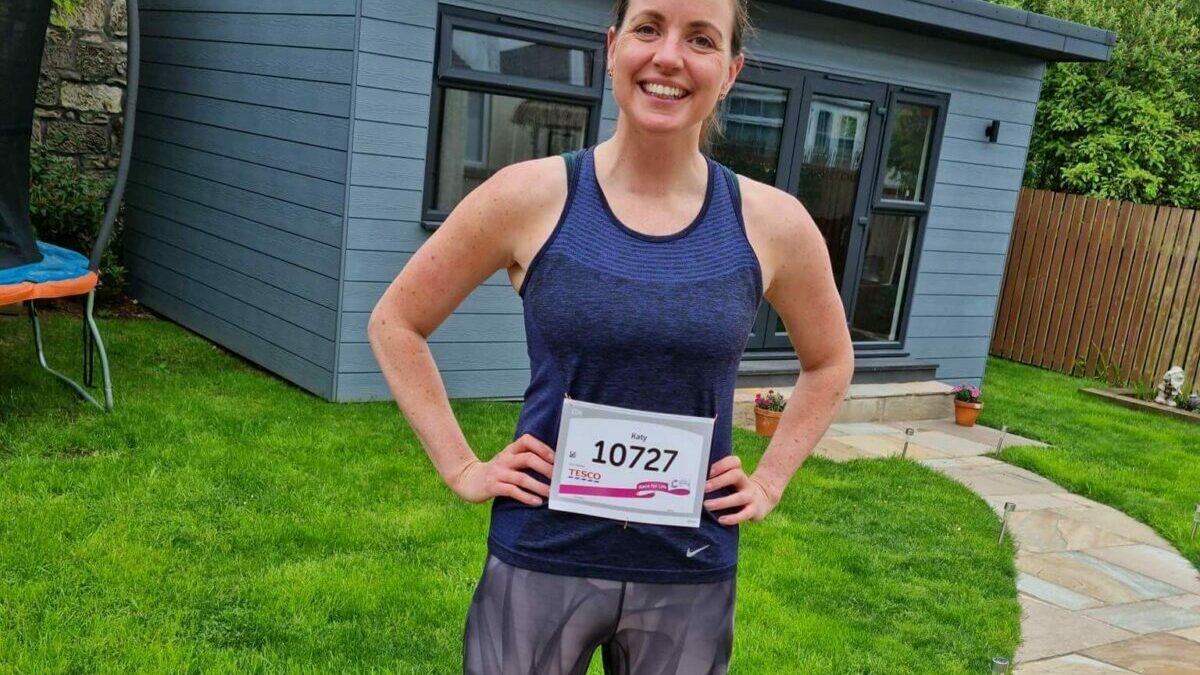 A woman standing in her garden in front of a shed wearing running clothes