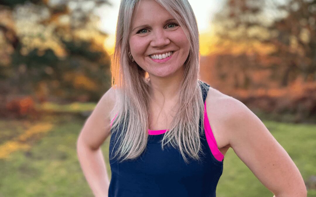 A woman standing in a garden with her hands on her hips looking into the camera wearing a gym vest