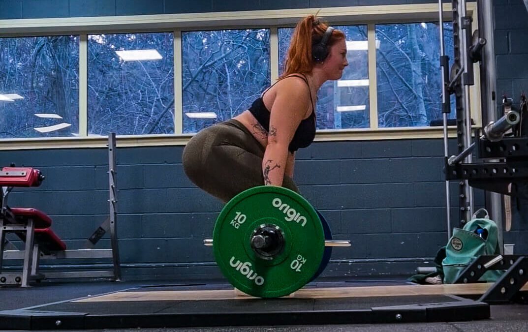 A woman lifting a heavy barbell facing sideways to the camera