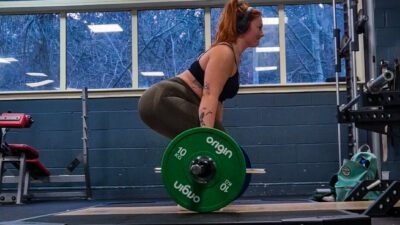 A woman lifting a heavy barbell facing sideways to the camera