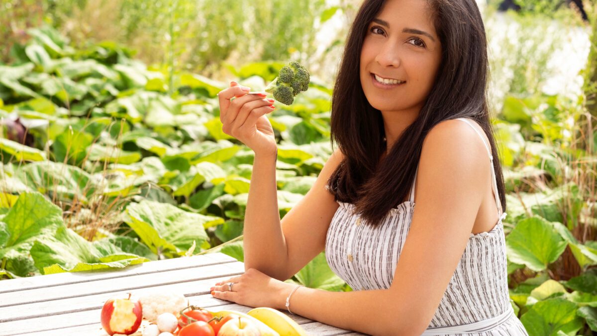 A woman with dark hair sitting at the table eating a broccoli