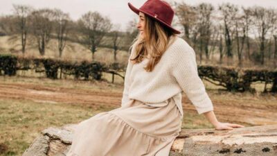 A woman facing away from the camera sitting on a felled tree wearing a hat