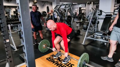 A man lifting a barbell from the floor wearing a red long sleeve shirt